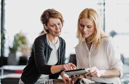 Two women seated together reviewing information on a tablet